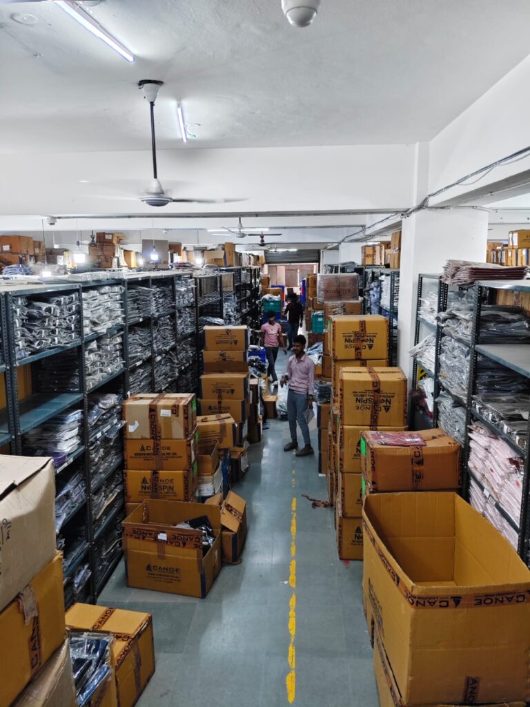 Warehouse staff working among organized shelves and shipping cartons while managing garment inventory and preparing customer orders.