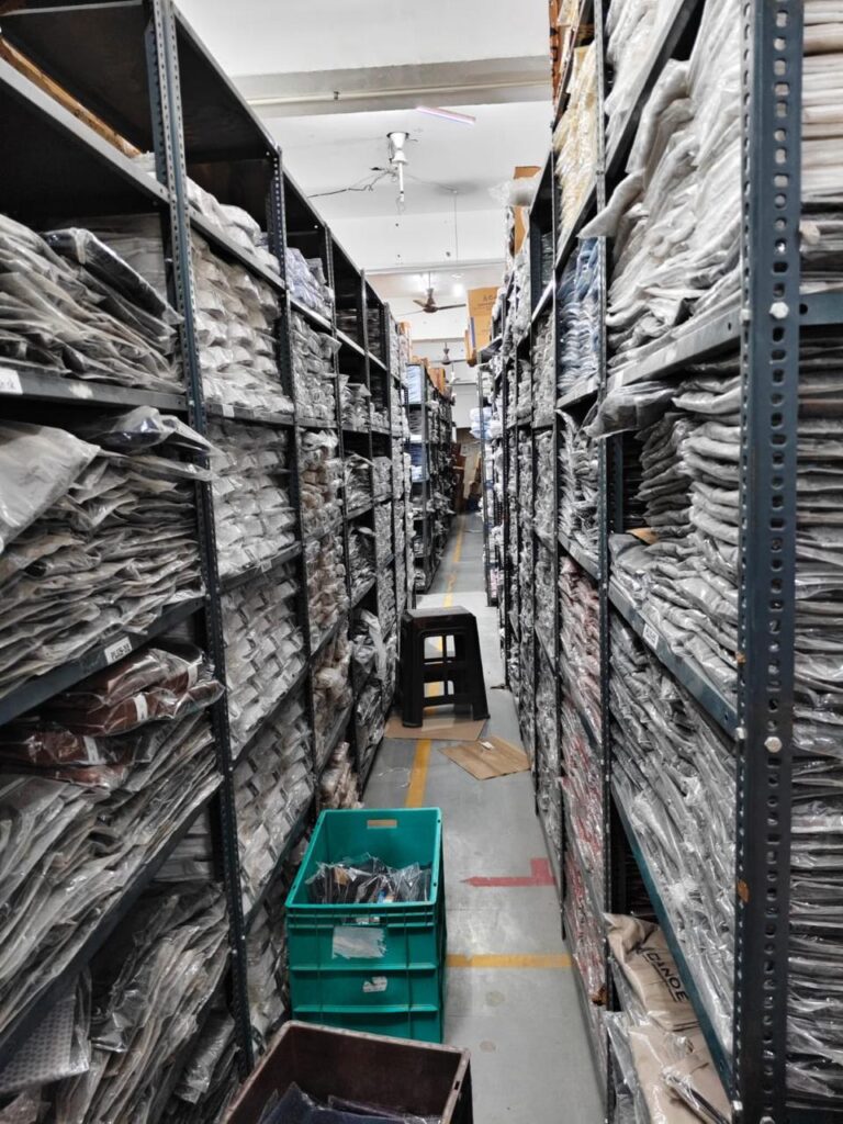A garment warehouse featuring storage racks, packed apparel, and plastic bins used for sorting and order preparation.