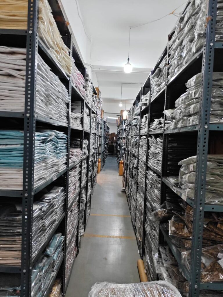 Long warehouse aisles with metal shelving stocked with neatly packed clothing inventory, providing efficient organization and easy product access.