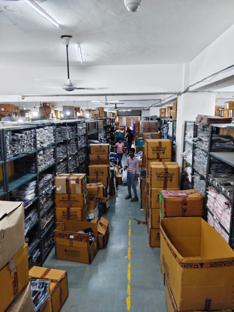 A busy apparel warehouse where staff members manage inventory and shipping boxes between storage racks filled with packaged clothing.